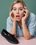 A blonde woman has a shocked expression on her face, looking at the black keds sneakers she ho...png