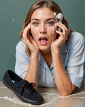 A blonde woman has a shocked expression on her face, looking at the black keds sneakers she ho...png