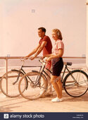 1950s-1960s-teen-couple-standing-by-bikes-on-beach-boardwalk-CMRBHW.jpg